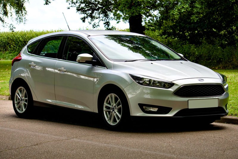 A sleek silver Ford Focus hatchback parked on a sunny day, with a scenic green background.