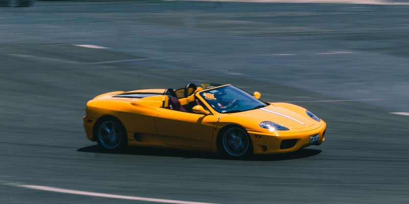 A vibrant yellow convertible sports car speeding on a racetrack, showcasing blurred motion and high speed.