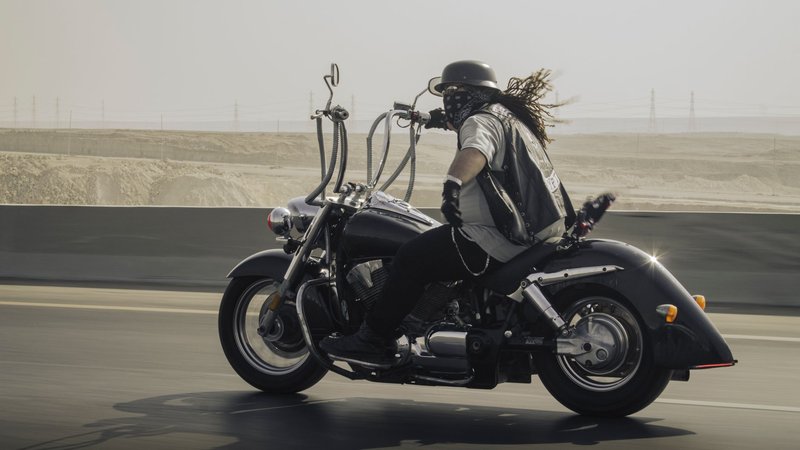 Biker in helmet and bandana rides a cruiser motorcycle on a sunny day.