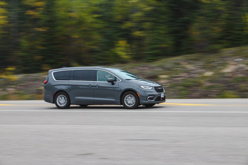 A modern minivan moving swiftly on a scenic highway surrounded by lush greenery.