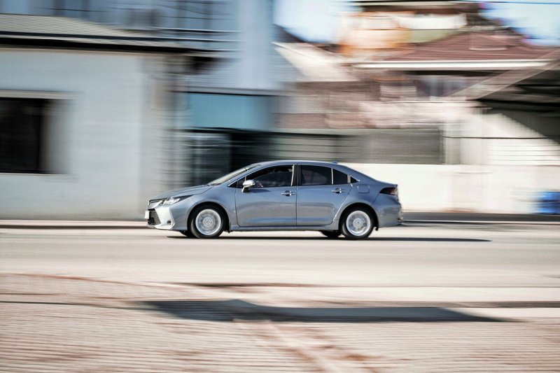 Dynamic capture of a gray sedan speeding down a city street with motion blur effect.
