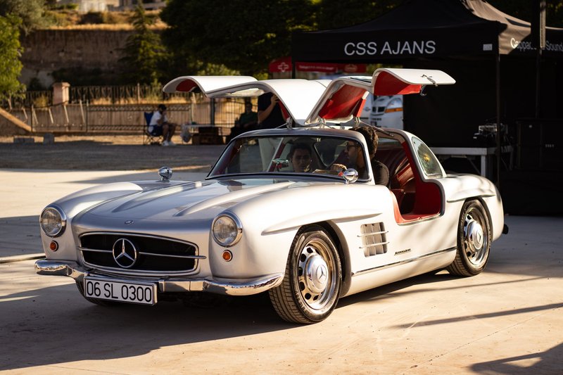 Silver Mercedes-Benz 300SL with iconic gullwing doors under sunlight at outdoor event.