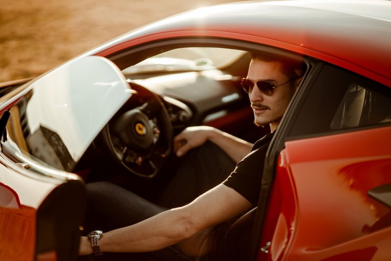 A stylish man sitting in a luxurious red sports car, enjoying the sunlight.