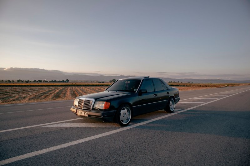 A vintage black car parked on an empty rural road at sunset, capturing serene countryside vibes.