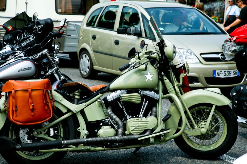 Classic army green motorcycle parked in a city alongside other vehicles.