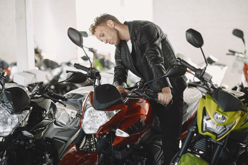 A man in a leather jacket checking motorcycles inside a dealership.