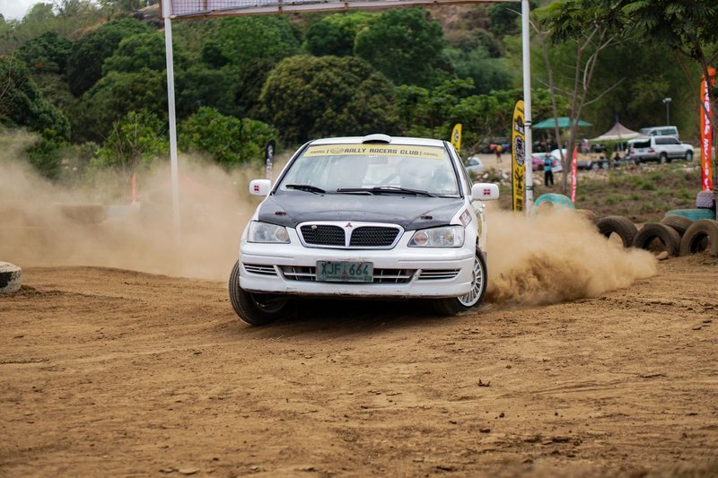 A rally car kicks up dust while drifting on a dirt track during a racing event.