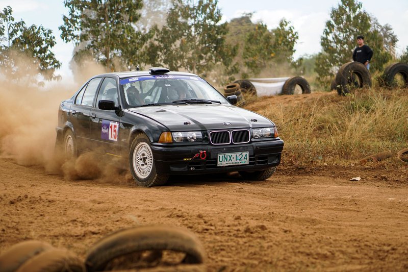 A car drifts through a dirt track during a high-speed race, kicking up dust.