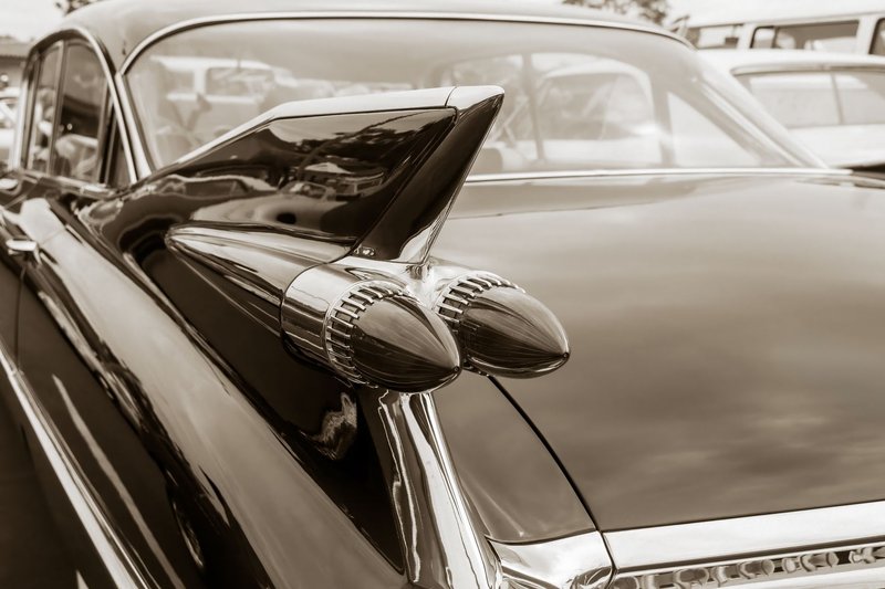 Elegant sepia close-up of a vintage car's iconic rear fin design.