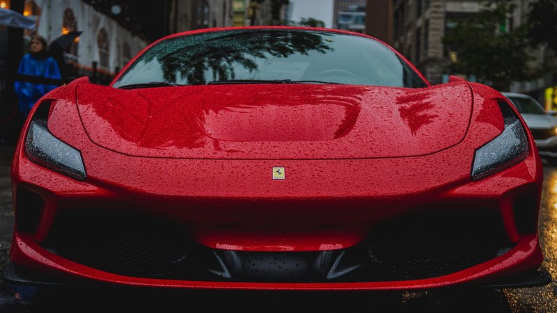 Front view of a vibrant red Ferrari parked on a rainy city street.