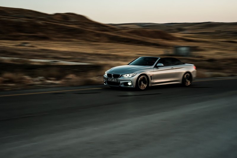A sleek silver convertible car captures motion on a highway, showcasing luxury and speed.