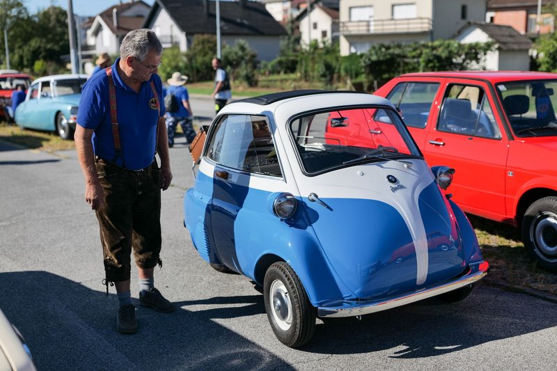 An elderly man admires a blue vintage Isetta microcar at a car show in Croatia.
