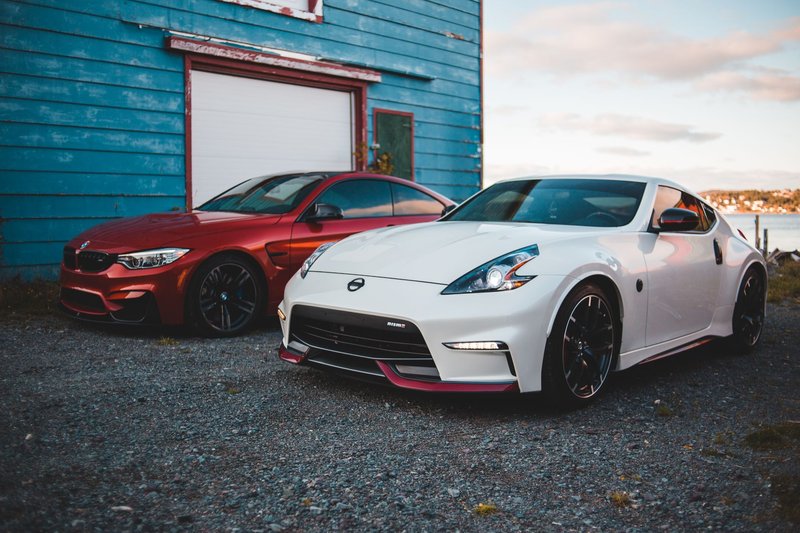 Stylish shiny tuned red and white sports cars parked near rustic barn at lakeside in suburb area