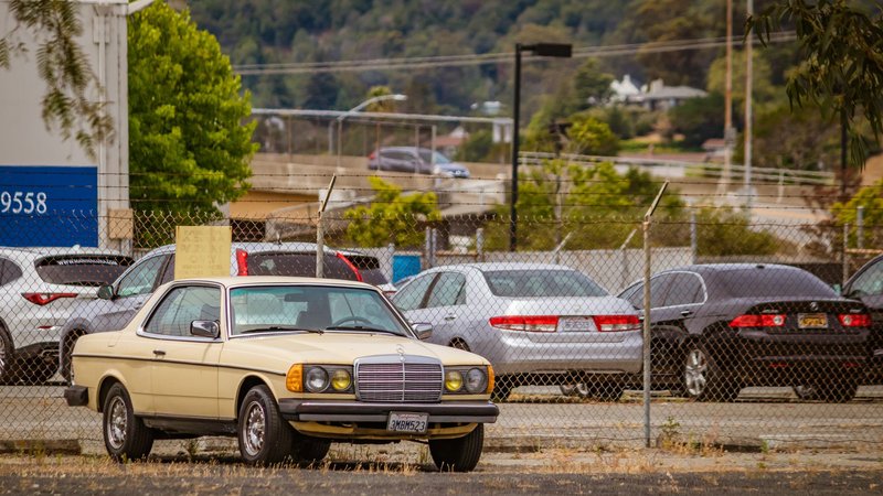 Classic Mercedes Benz parked in a fenced urban parking area with various cars in background.