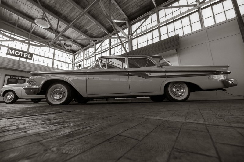 Black and white image of vintage 1950s cars in an indoor showroom, nostalgic atmosphere.