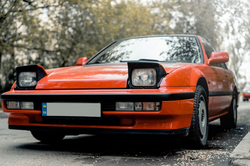 A vibrant red sports coupe parked outdoors, showcasing classic headlights and design.