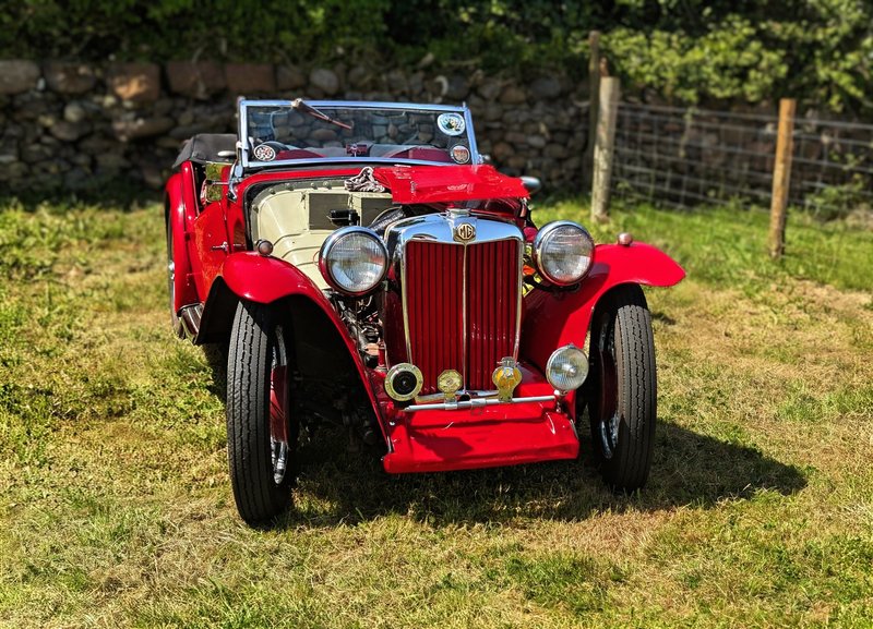 Classic red MG sports car parked on grass, highlighting its vintage charm and sleek design.