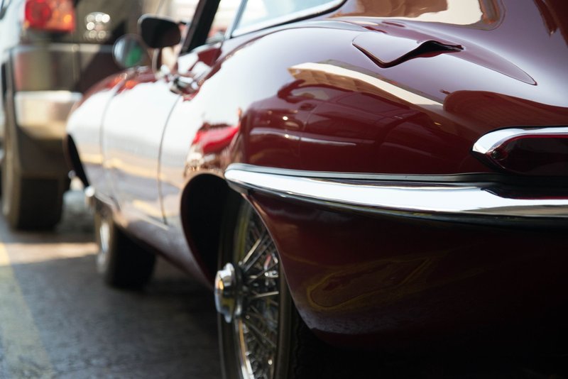 Close-up of a classic Jaguar XK E coupe with shiny chrome details parked in an urban setting.