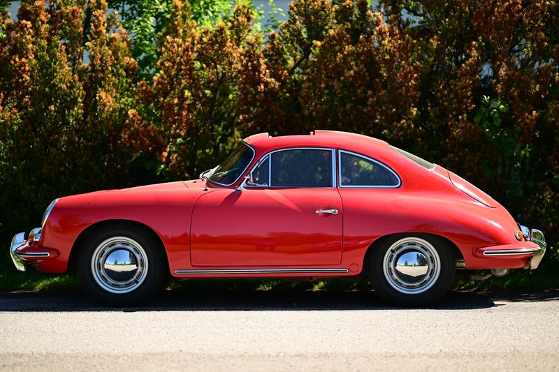 Classic red sports car parked by lush greenery on a sunny day in Uusimaa, Finland.