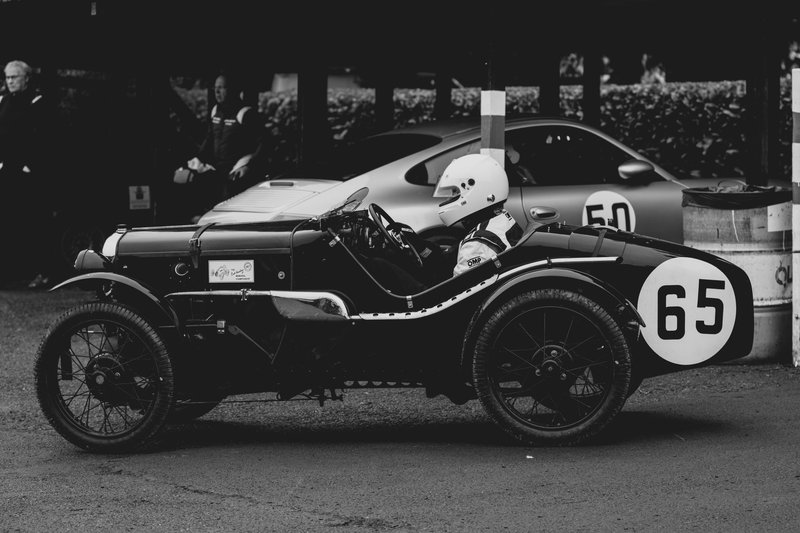 Side view of a vintage racing car at a historic European motorsport event in black and white.