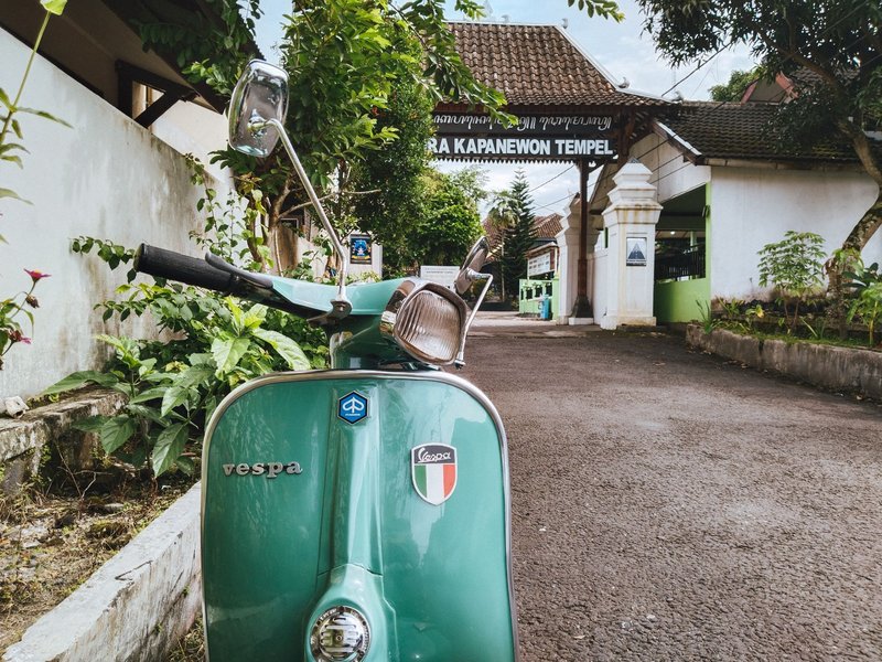 Retro Vespa scooter parked by gate in Jogja, Indonesia, showcasing nostalgic travel vibes.