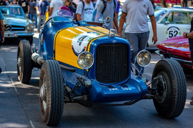 Colorful vintage racing car on display at an outdoor car gathering, surrounded by people.