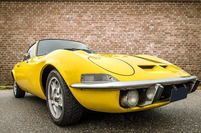 Classic yellow vintage coupe car in front of a red brick wall. Perfect for automotive enthusiasts.