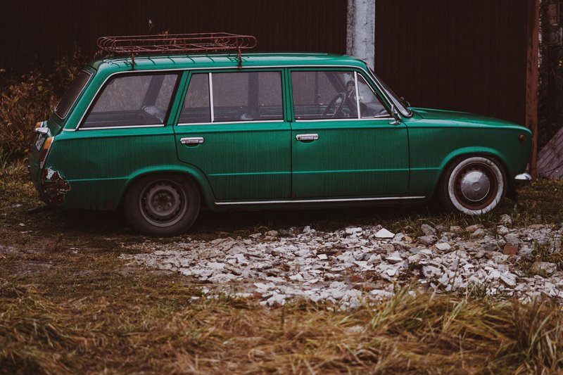 Retro green station wagon parked on gravel with rust detailing.
