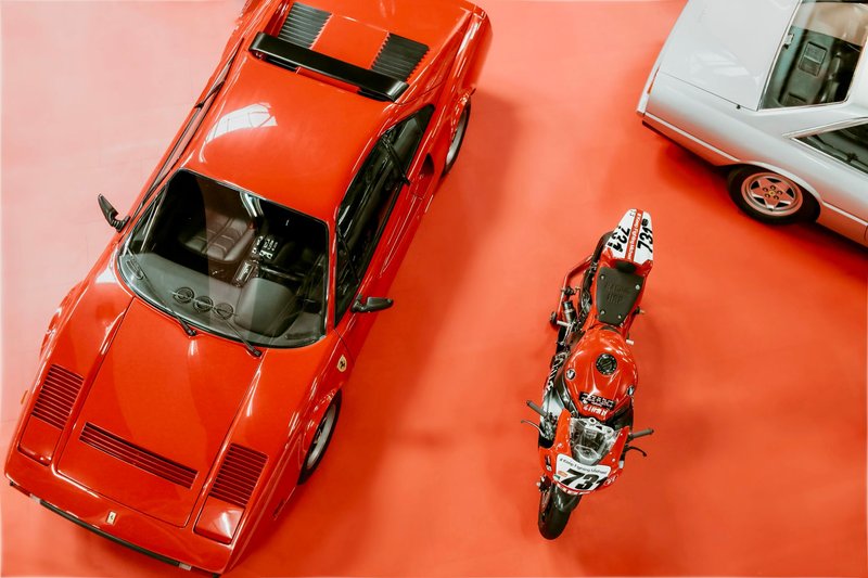 High angle shot of classic Ferrari and motorcycle on display at an automotive exhibition.