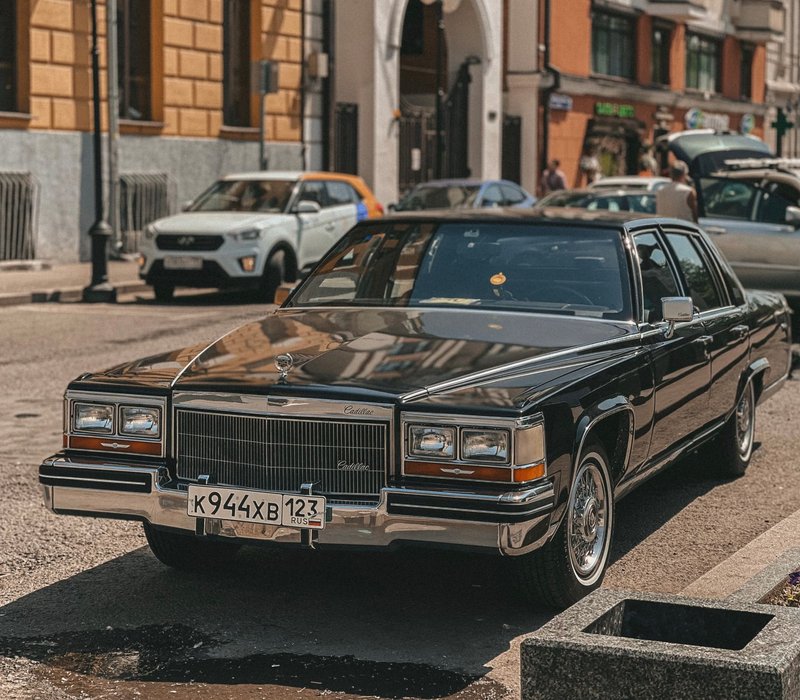 A classic black Cadillac parked on a sunny urban street, showcasing vintage elegance.