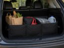 A black three-compartment trunk organizer holding groceries, jumper cables, a blanket and a water jug in the cargo area of an SUV