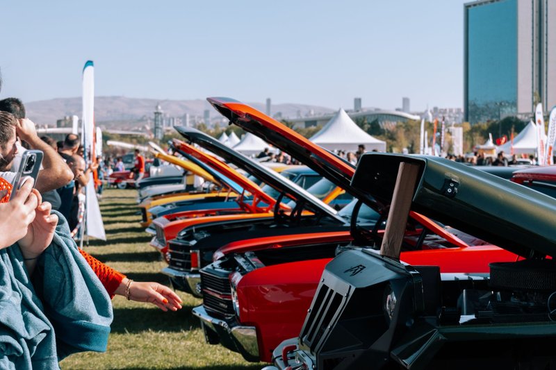 Lineup of vintage cars with open hoods at an outdoor car show, attracting a crowd.