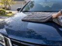 Gray twisted loop microfiber drying towel pulled across the wet hood of a dark blue sedan