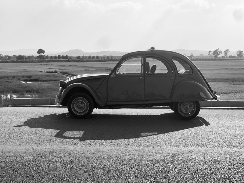 Black and white side view of a classic Citroen 2CV parked on a rural road in Antananarivo.