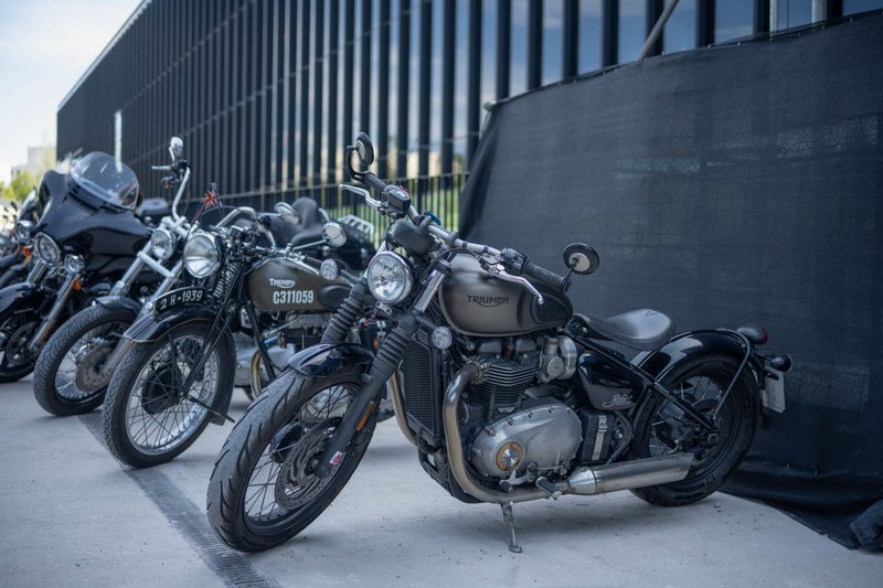 Lineup of Triumph motorcycles parked outdoors with modern architecture backdrop.