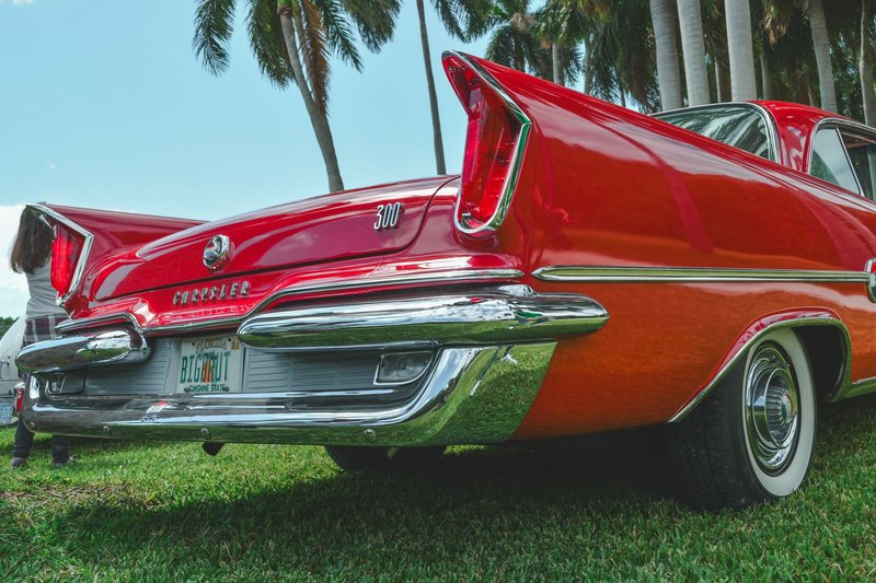 Classic red Chrysler car parked on grass under palm trees on a sunny day.