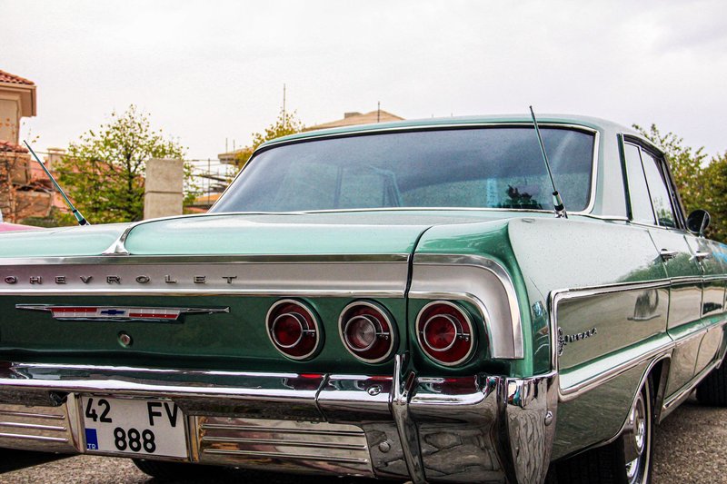 Classic green Chevrolet Impala parked outdoors showcasing chrome and vintage taillights.
