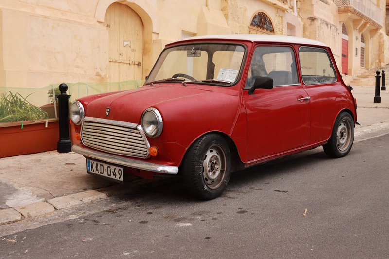 A classic red Mini car parked on a traditional street in Malta, showcasing vintage charm.