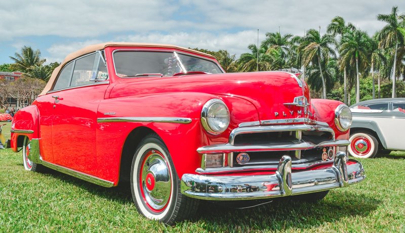 Classic red Plymouth convertible on display outdoors with palm trees in the background.