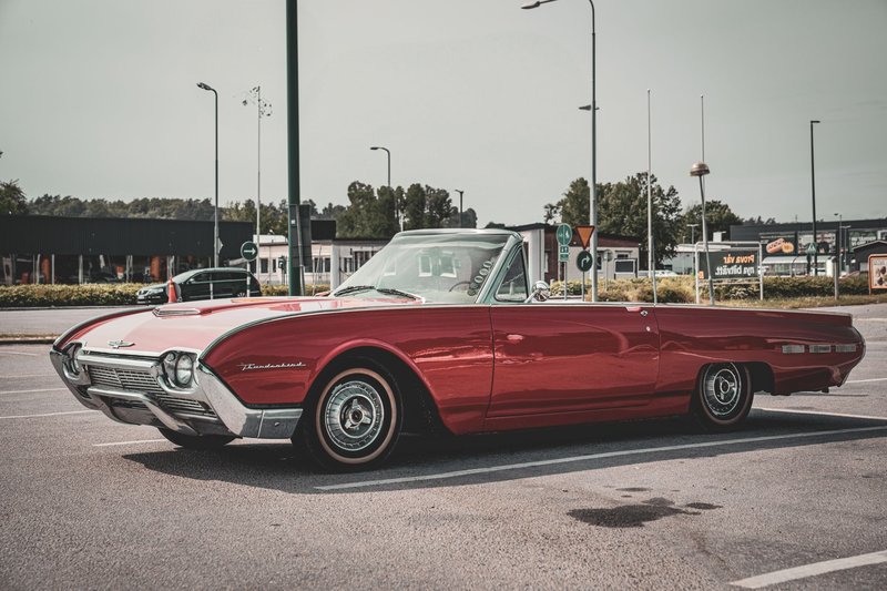Vintage red Ford Thunderbird parked in a sunny urban location, showcasing classic design and style.