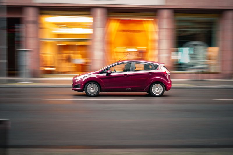 Dynamic shot of a red compact car speeding on a city street with a blurred background.