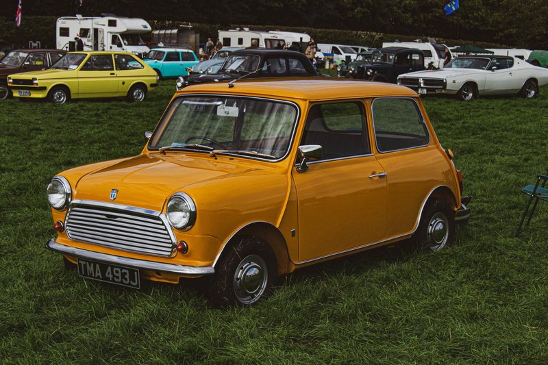 Bright orange vintage Mini car showcased at an outdoor car rally on a grassy field.