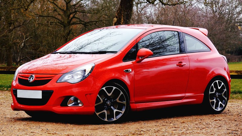 A vibrant red coupe car parked outdoors against a scenic UK countryside backdrop.