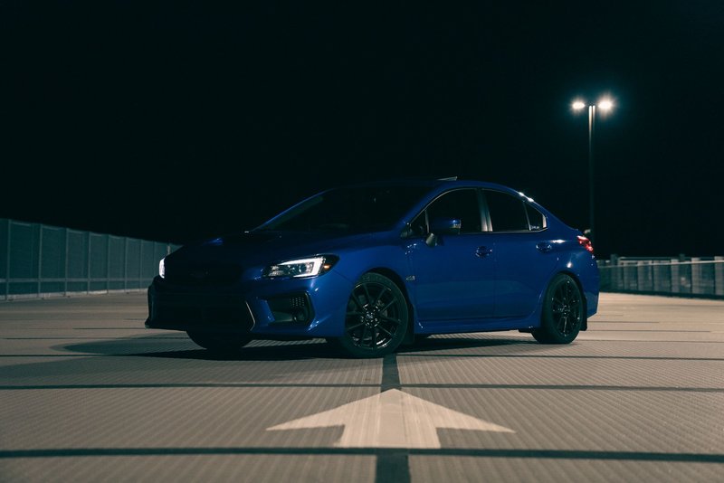 A stylish blue sedan car angled front view under streetlights on an empty parking lot at night.