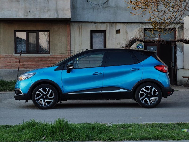 A blue compact SUV is parked on a city street beside an old building.