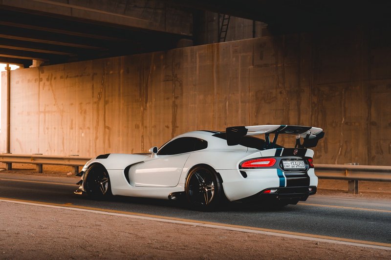 White sports car with blue stripes racing through a tunnel at sunset.