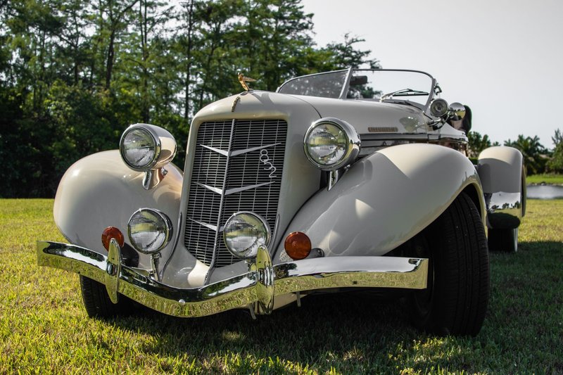Front view of a vintage cream-colored automobile on grass under clear skies.