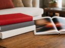 A stack of large hardcover books beside an open photo book on a wooden coffee table
