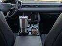 A large steel tumbler in a cup holder expander next to a coffee cup and a cup holder phone mount in a car console