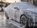 Gray sedan in a driveway covered in thick white snow foam from a foam cannon